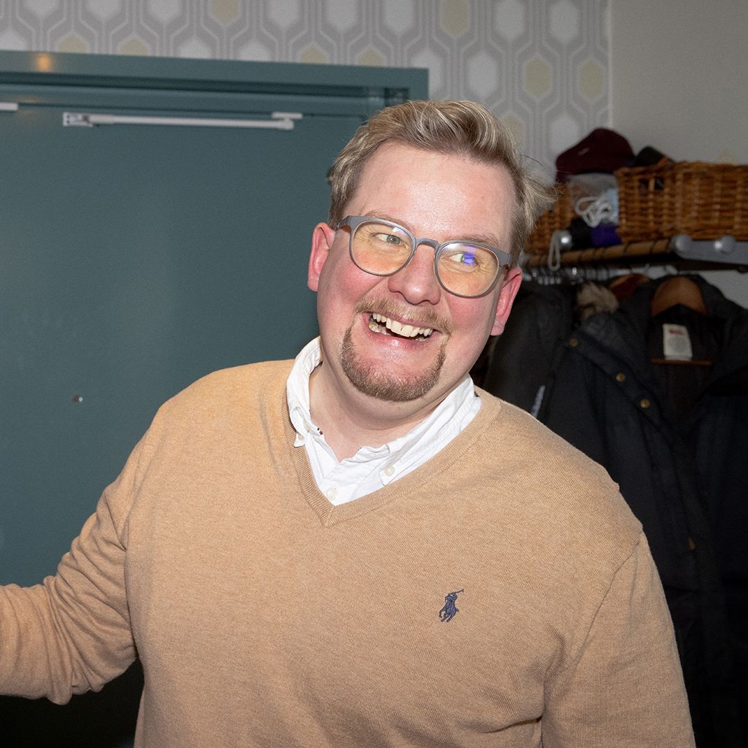 En man med glasögon som står i en hal och funderar på hur han ska spara pengar.